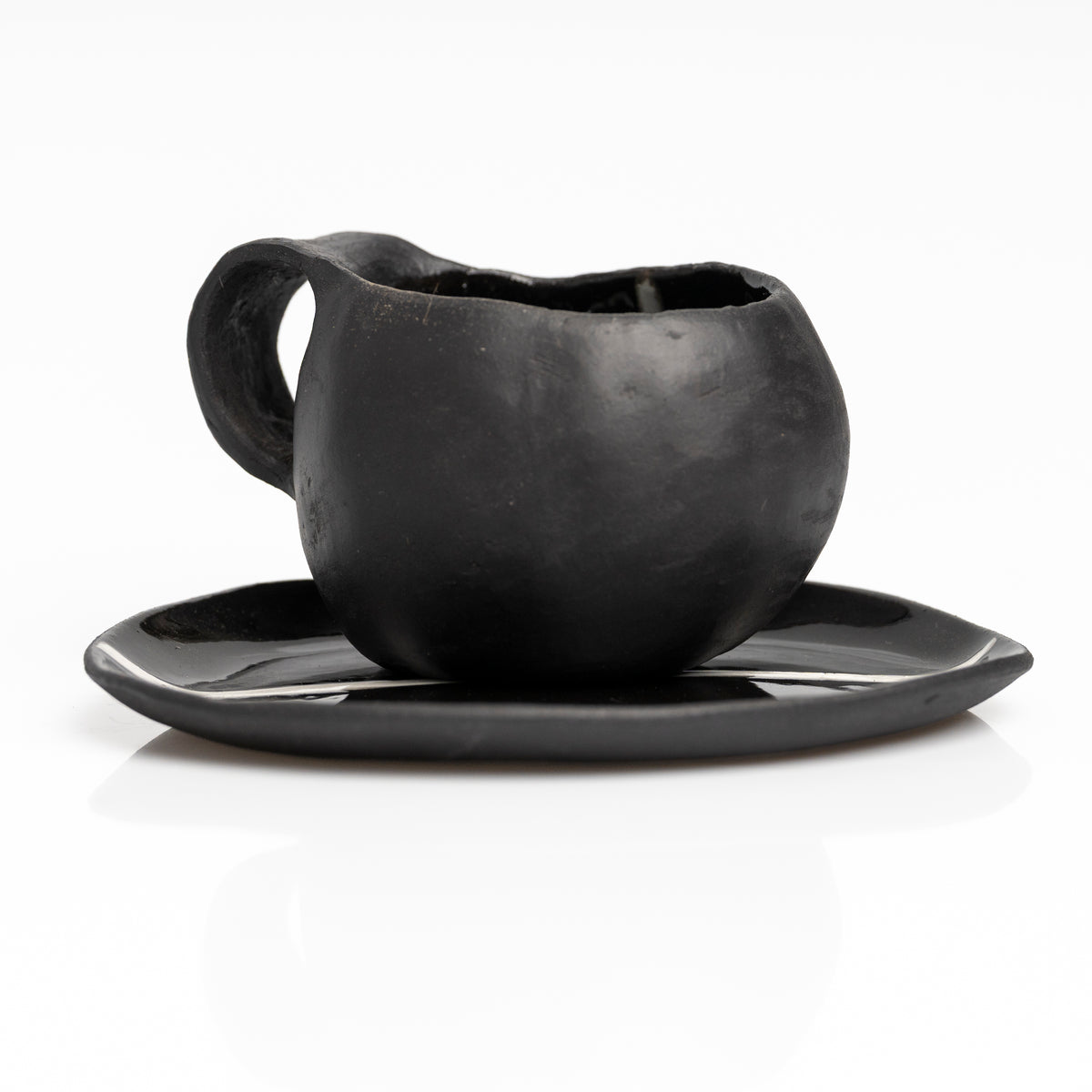     Handmade black stoneware coffee cup and saucer with white line detail.