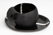     Handmade black stoneware coffee cup and saucer with white line detail.